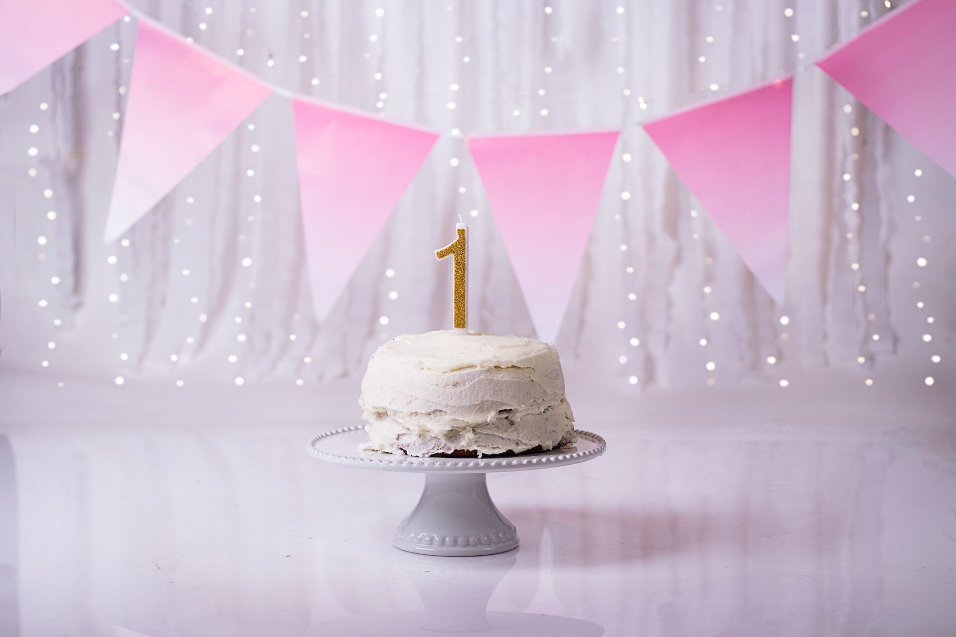 White birthday cake with a golden candle in the shape of the number 1