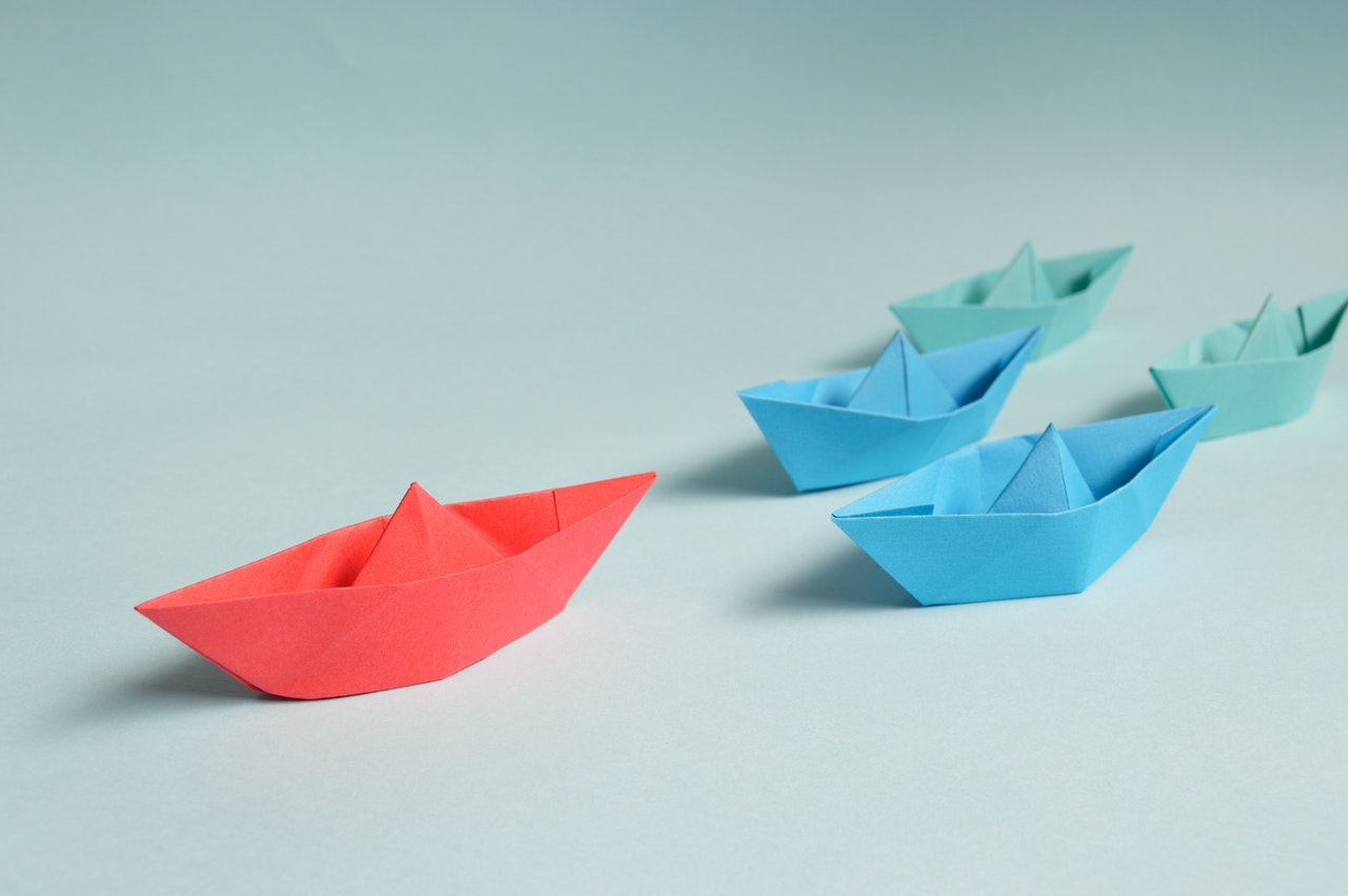 Paper boats in a v-shaped formation with a red boat leading the way
